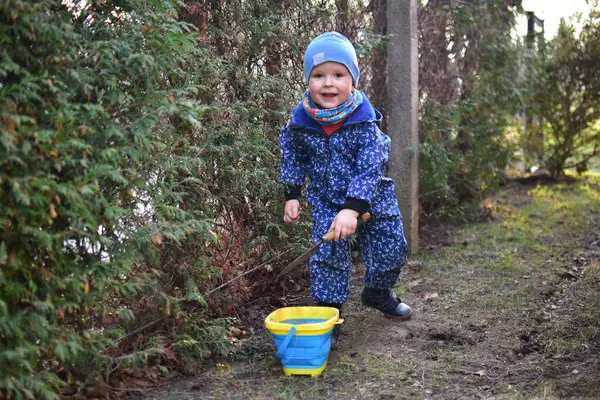 Mavi, yumuşak kabuklu mayolu çocuk baharda güneşli bir günde bahçedeki bir kovaya toprak kazıyor..