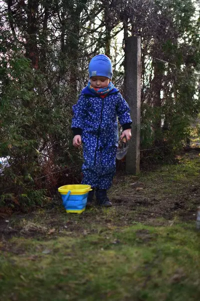 Mavi, yumuşak kabuklu mayolu çocuk baharda güneşli bir günde bahçedeki bir kovaya toprak kazıyor..