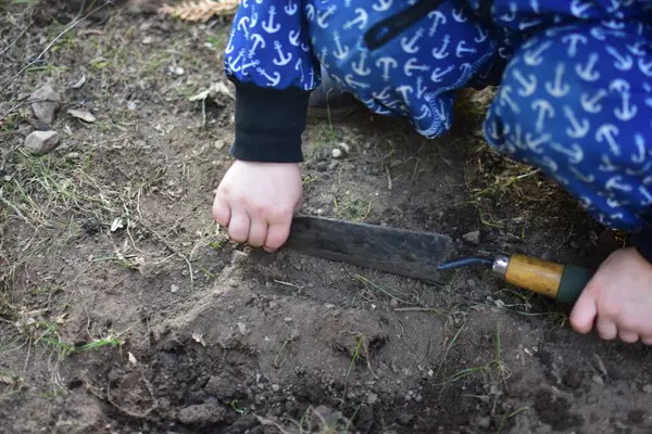 Mavi, yumuşak kabuklu mayolu çocuk baharda güneşli bir günde bahçenin arka bahçesinde çukur kazarak toprak kazıyor. .