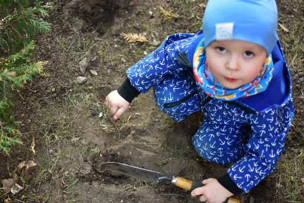 Mavi, yumuşak kabuklu mayolu çocuk baharda güneşli bir günde bahçenin arka bahçesinde çapa kazıyor..