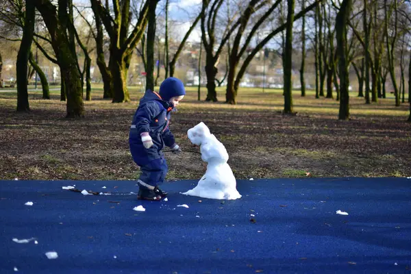 İlkbaharda şehir parkında çocukların parkındaki son kardan adam yapan çocuk. Çocuk ve üzgün görünümlü kardan adam kışın bitmesini bekliyor..
