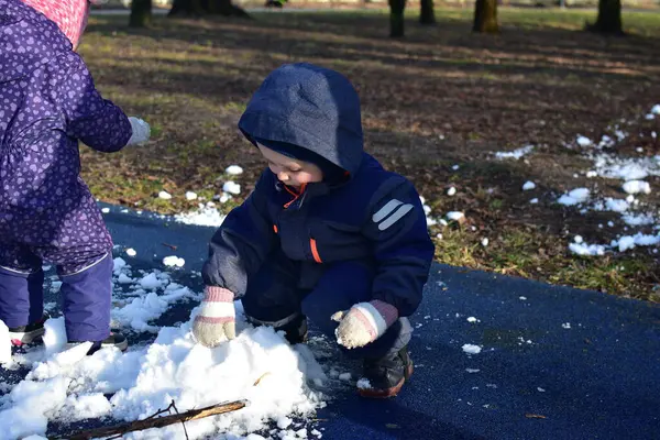 Küçük çocuk ve kız kardan adam yapmak için parkta oynuyorlar güneşli bahar zamanı. Erkek ve kız kardeş bahar zamanı son karla oynuyorlar..