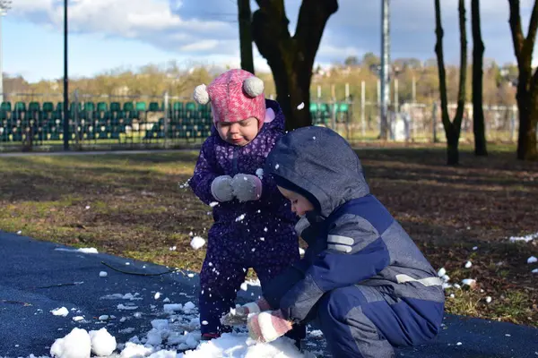 Küçük çocuk ve kız güneşli bahar zamanı parkta karla oynuyorlar. Erkek ve kız kardeş bahar zamanı son karla oynuyorlar..