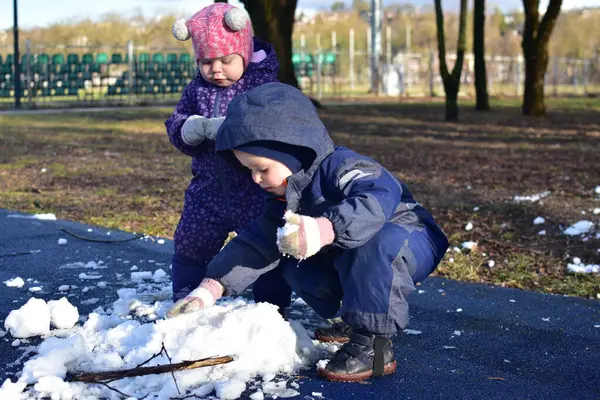 Küçük çocuk ve kız güneşli bahar zamanı parkta karla oynuyorlar. Erkek ve kız kardeş bahar zamanı son karla oynuyorlar..