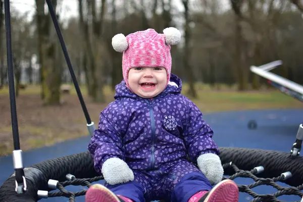 Soğuk sonbaharda, şehir parkında çocuk parkında sallanan bir kız bebek. Küçük kız kışın halk parkında eğleniyor.