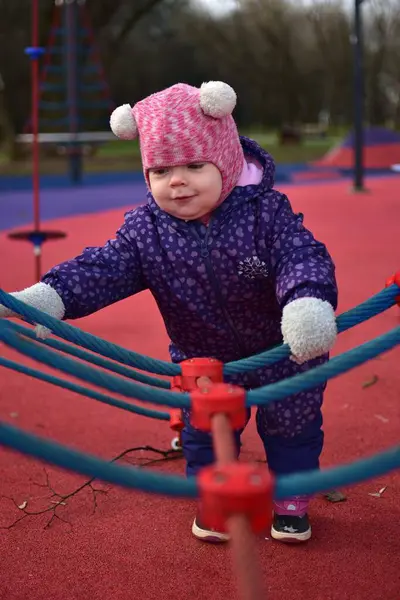 Yavru kız gülümsüyor ve buz gibi baharda parktaki çocuk parkında ip tırmanışı yapıyor. Küçük kız kışın halk parkında eğleniyor..