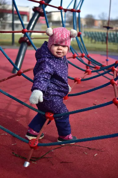 Yavru kız gülümsüyor ve buz gibi baharda parktaki çocuk parkında ip tırmanışı yapıyor. Küçük kız kışın halk parkında eğleniyor..