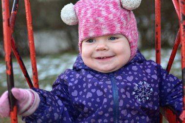 Soğuk havada sovyet tarzı çocuk parkında sallanan küçük bir kız çocuğu. Küçük kız kışın halk parkında eğleniyor.