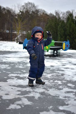 Küçük çocuk halka açık parkta parktaki parlayan kollarıyla buza dokunuyor. Kışın soğuk havada dışarıda oynayan bir çocuk..