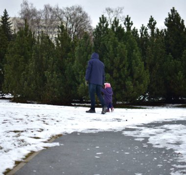 Babası, şehir parkında soğuk kış mevsiminde küçük kızlarının elini tutuyor. Baba ve kızı dışarıda beraber yürüyorlar..