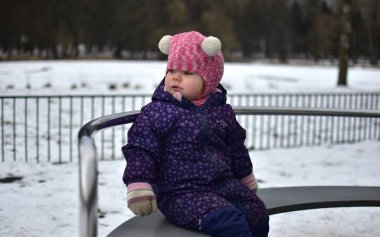 Yavru kız soğuk sonbaharda parktaki çocuk parkında oynayıp eğleniyor. Küçük kız kışın halk parkında eğleniyor.