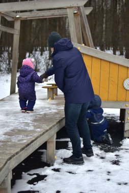 Babası şehir parkında kışın soğuk havasında küçük kızı ve oğluyla oynuyor. Baba ve çocuklar birlikte vakit geçiriyorlar. Babam küçük kızlarının elini tutuyor..