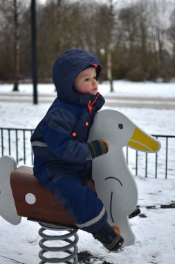 Küçük çocuk soğuk kış havasında çocuk parkında kaz sandalyesinde oturuyor..