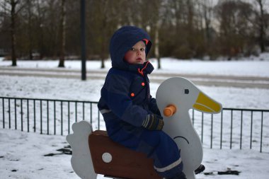 Küçük çocuk soğuk kış havasında çocuk parkında kaz sandalyesinde oturuyor..