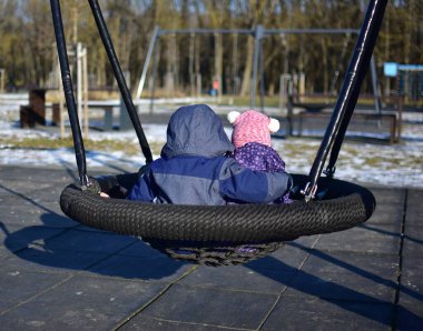 Erkek ve kız kardeş şehir parkında birlikte sallanıyorlar. İki kardeş arasındaki güçlü bağ kavramı. Erkek kardeşi küçük kız kardeşine sarılıyor. İki çocuk arkada oturuyor. Kardeşlerin sevgisi..