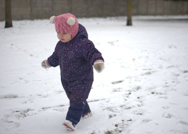 Soğuk kışta karda yürüyen küçük bir kız. Küçük kız kışın dışarıda eğleniyor..