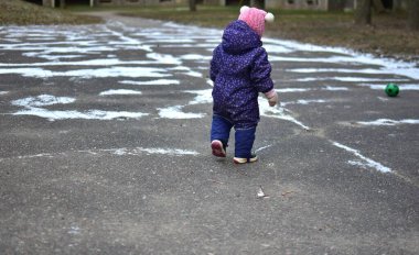 Yavru kız soğuk kış mevsiminde dışarıda küçük toplarla oynuyor. Küçük kız kışın dışarıda eğleniyor..