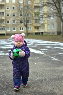 Yavru kız soğuk kış mevsiminde dışarıda küçük toplarla oynuyor. Küçük kız kışın dışarıda eğleniyor..