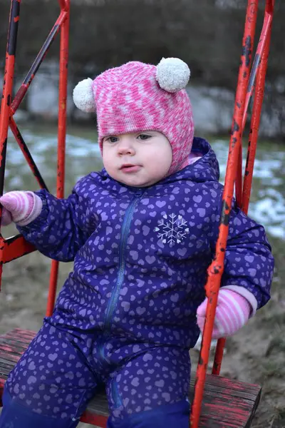 Soğuk havada sovyet tarzı çocuk parkında sallanan küçük bir kız çocuğu. Küçük kız kışın halk parkında eğleniyor.