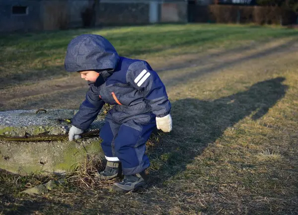 Sonbaharda şehirde eski atık yönetimini izleyen kapüşonlu meraklı bir çocuk. Yürüyen çocuk drenajın yanında duruyor ve beton cephaneliğe dokunuyor..