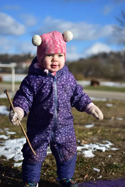 Yavru kız mutlu bir şekilde gülümsüyor ve soğuk sonbaharda şehir parkındaki çocuk parkında oynuyor. Küçük kız kışın halk parkında eğleniyor.