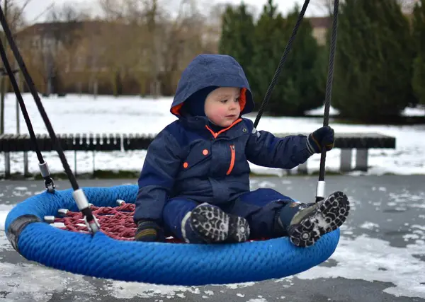 Soğuk sonbaharda çocuk parkında sallanan bir çocuk. Küçük çocuk kışın halk parkında eğleniyor..