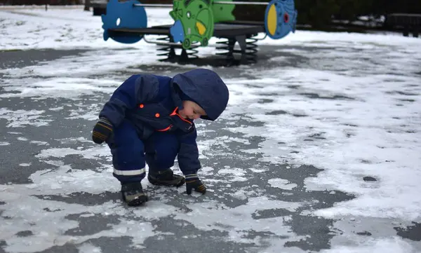 Küçük çocuk halka açık parkta parktaki parlayan kollarıyla buza dokunuyor. Kışın soğuk havada dışarıda oynayan bir çocuk..