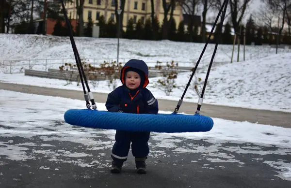 Soğuk sonbaharda çocuk parkında sallanan bir çocuk. Küçük çocuk kışın halk parkında eğleniyor..