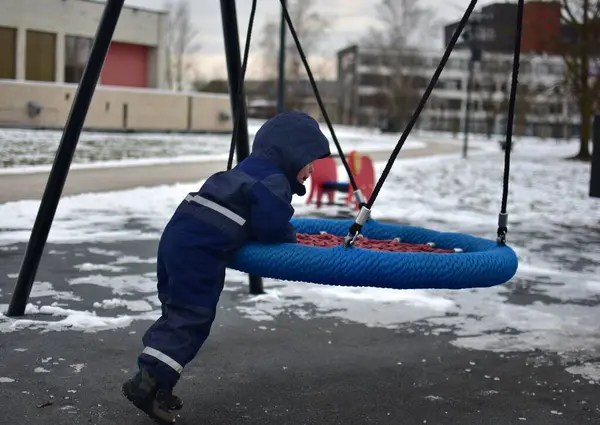 Soğuk sonbaharda çocuk parkında sallanan bir çocuk. Küçük çocuk kışın halk parkında eğleniyor..