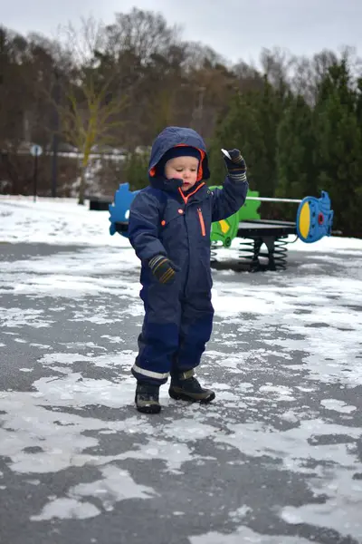Küçük çocuk halka açık parkta parktaki parlayan kollarıyla buza dokunuyor. Kışın soğuk havada dışarıda oynayan bir çocuk..