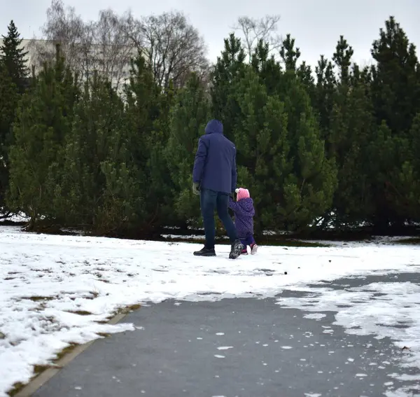 Babası, şehir parkında soğuk kış mevsiminde küçük kızlarının elini tutuyor. Baba ve kızı dışarıda beraber yürüyorlar..