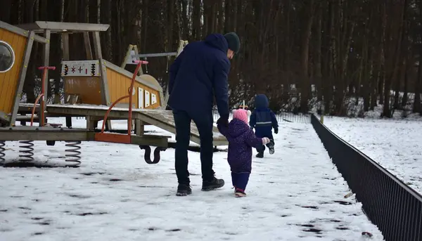 Erkek kardeş, kız kardeş ve baba soğuk kış havasında çocuk parkında oynuyorlar. Çocuklarla dışarıda ailece vakit geçirmek..