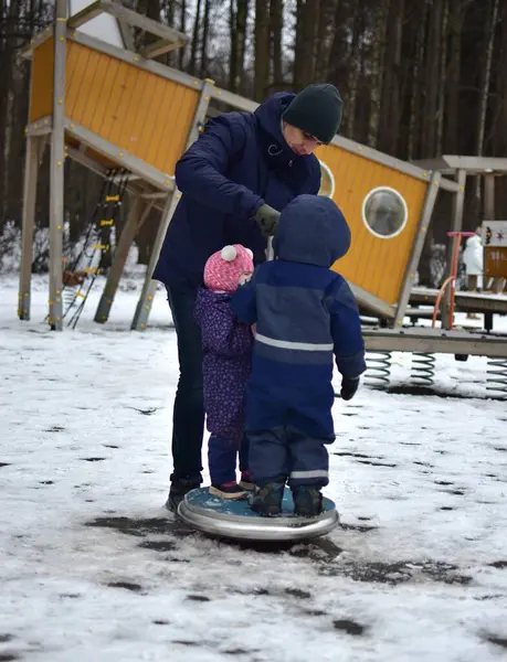 Erkek kardeş, kız kardeş ve baba soğuk kış havasında çocuk parkında oynuyorlar. Çocuklarla dışarıda ailece vakit geçirmek. Kardeşler oyun alanındaki ekipmanların üzerinde duruyor ve etrafta dönüyorlar..