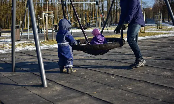Baba ve oğul, soğuk kış günlerinde çocuklarını çocuk parkında sallandırıyor. Baba ve çocuklar birlikte vakit geçiriyorlar..