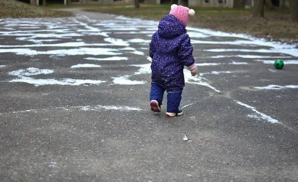 Yavru kız soğuk kış mevsiminde dışarıda küçük toplarla oynuyor. Küçük kız kışın dışarıda eğleniyor..
