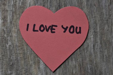 Tahta döşemeli arka planda, sevgililer günü için kırmızı kalp şeklindeki kağıtta seni seviyorum mesajı. Sevgililer günü kartında seni seviyorum yazıyor. Minimalist Sevgililer Günü.