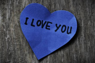 Seni mavi kalp şeklindeki kağıt kartta seviyorum. Tahta ahşap kaplamalı arkaplanda sevgililer günü için. Sevgililer günü kartında seni seviyorum yazıyor. Minimalist Sevgililer Günü.