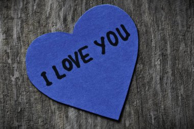 Seni mavi kalp şeklindeki kağıt kartta seviyorum. Tahta ahşap kaplamalı arkaplanda sevgililer günü için. Sevgililer günü kartında seni seviyorum yazıyor. Minimalist Sevgililer Günü.