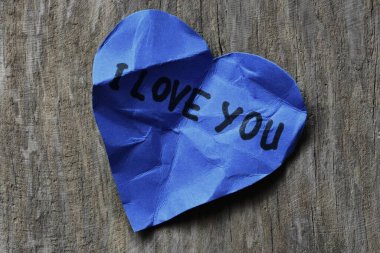 Tahta desenli arka planda sevgililer günü için buruşuk mavi kalp şeklinde kağıt üzerinde seni seviyorum mesajı. Kırık Sevgililer Günü kartında seni seviyorum yazıyor. Reddedilmiş sevgililer günü tebrikleri..
