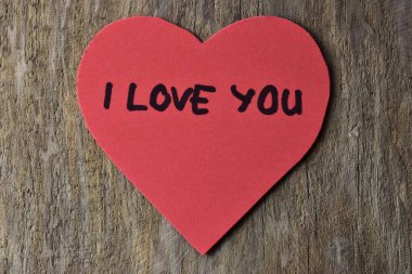 Tahta döşemeli arka planda, sevgililer günü için kırmızı kalp şeklindeki kağıtta seni seviyorum mesajı. Sevgililer günü kartında seni seviyorum yazıyor. Minimalist Sevgililer Günü.