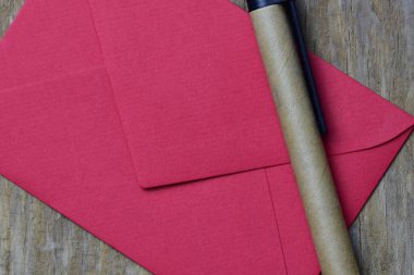 Ahşap arka planda küçük kırmızı bir zarf ve geri dönüştürülmüş kağıttan yapılmış sürdürülebilir kalem. Minimalist Sevgililer Günü kartı.