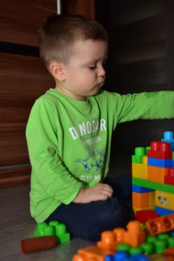 Küçük çocuk evde renkli bloklarla oynuyordur. Küçük çocuk konsantre ve blok kale inşa ediyor gibi görünüyor. Küçük çocuk inşaat oyuncaklarıyla oynayarak yaratıcılığını geliştiriyor..