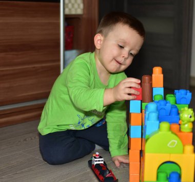 Küçük çocuk evde renkli bloklarla oynuyordur. Küçük çocuk konsantre ve blok kale inşa ediyor gibi görünüyor. Küçük çocuk inşaat oyuncaklarıyla oynayarak yaratıcılığını geliştiriyor..