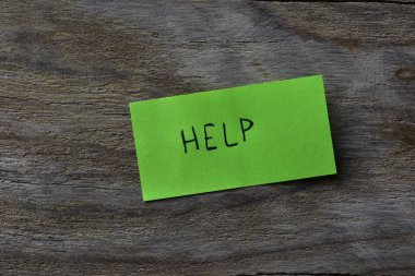 Tahta döşemeli arka plandaki yeşil yapışkan nota mesaj yardımı. Not kağıdına kelime yardımı yazan bir kalem.