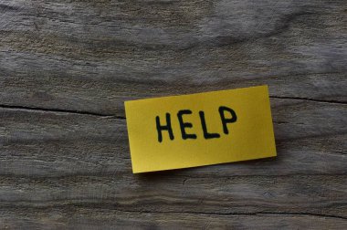 Tahta döşemeli arka plandaki sarı yapışkan nota mesaj yardımı. Siyah kalem not kağıdına kelime yardımı yazdı.