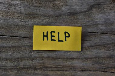 Tahta döşemeli arka plandaki sarı yapışkan nota mesaj yardımı. Siyah kalem not kağıdına kelime yardımı yazdı.