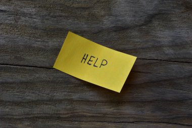 Tahta döşemeli arka plandaki sarı yapışkan nota mesaj yardımı. Not kağıdına kelime yardımı yazan bir kalem.