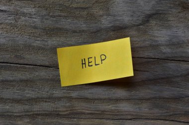 Tahta döşemeli arka plandaki sarı yapışkan nota mesaj yardımı. Not kağıdına kelime yardımı yazan bir kalem.