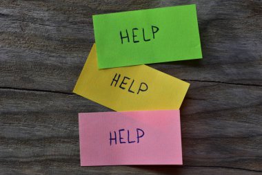 Tahta kaplamalı arka planda pembe yeşil ve sarı yapışkan notlar için mesaj yardımı. Not kağıdına kelime yardımı yazan bir kalem.