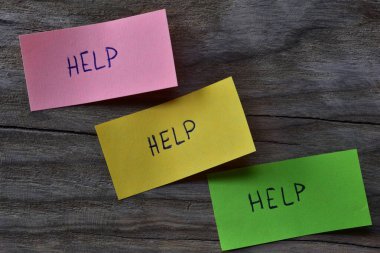 Tahta kaplamalı arka planda pembe yeşil ve sarı yapışkan notlar için mesaj yardımı. Not kağıdına kelime yardımı yazan bir kalem.